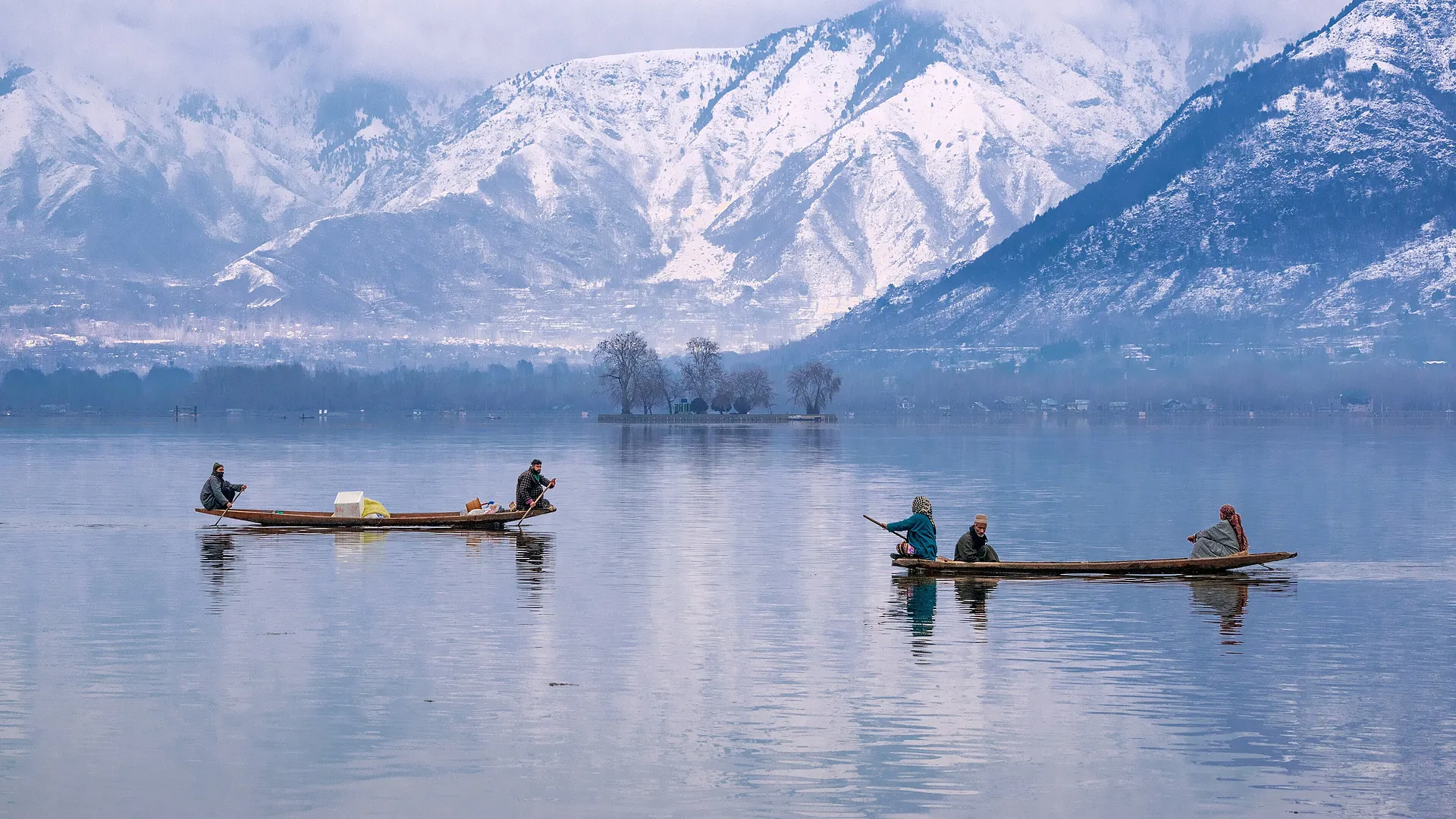 Shikaras on a calm lake beneath snowy mountains in Kashmir